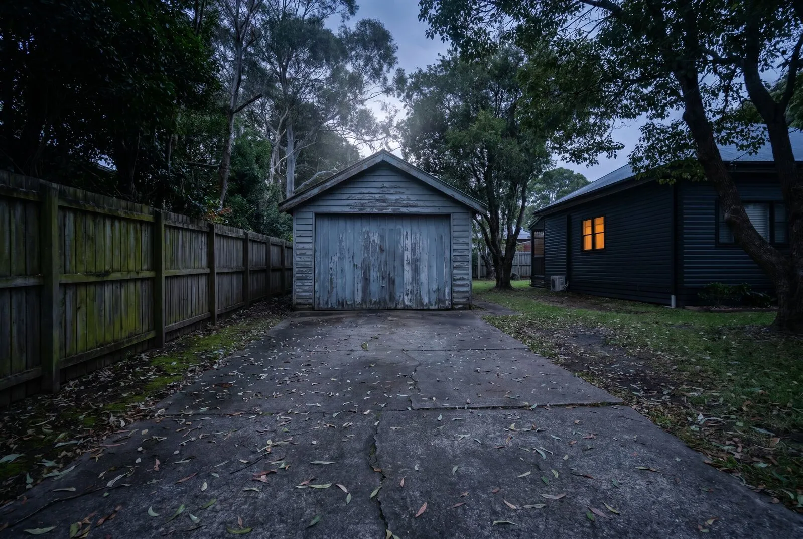 An original detached garage with an old tilt door at the end of a narrow side driveway beside a renovated bungalow