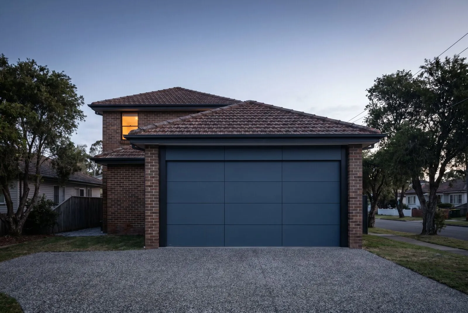 A new flat-profile sectional garage door installed on a renovated post-war brick-and-tile house in early morning light