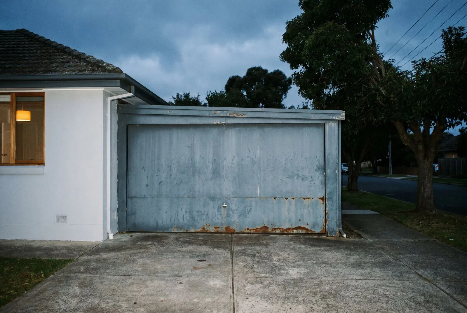 A tired 1970s tilt garage door with faded paint beside a freshly renovated house facade
